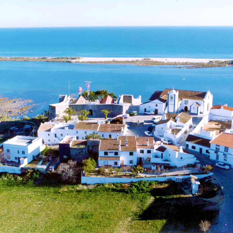 Cacela Velha seen from above: whitewashed houses, a fortress and a church on a low bluff, with the Ria Formosa lagoon and its sandbar beyond