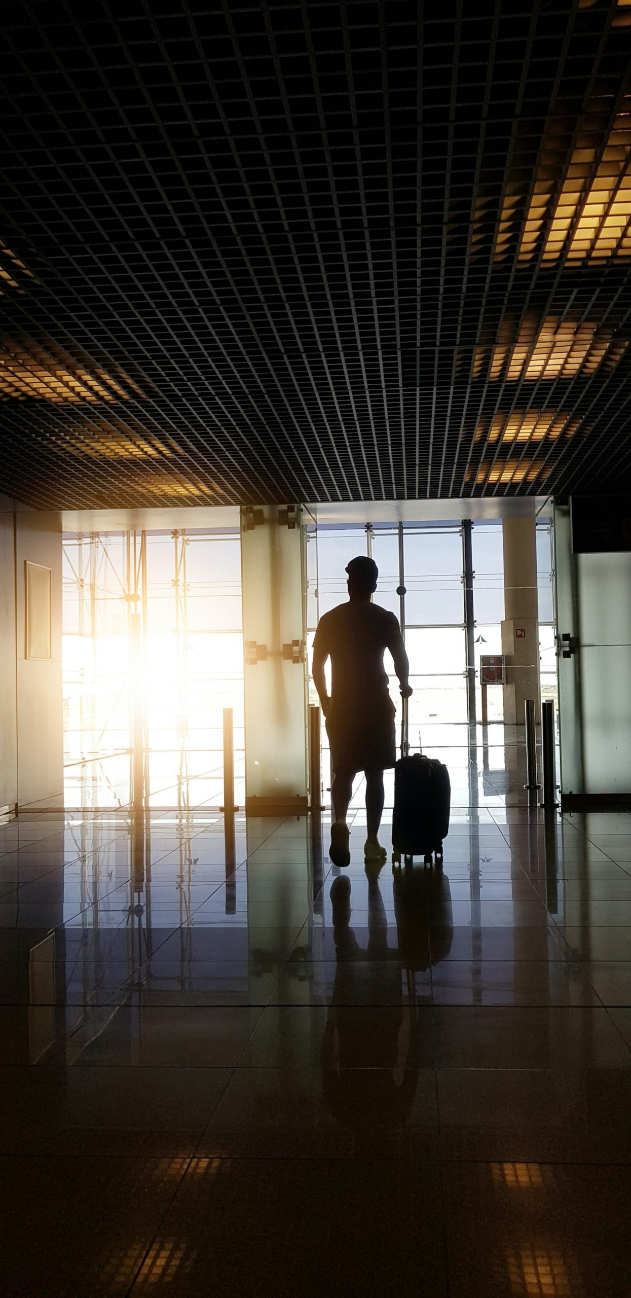 A traveller silhouetted against the light, walking through an airport terminal with a suitcase